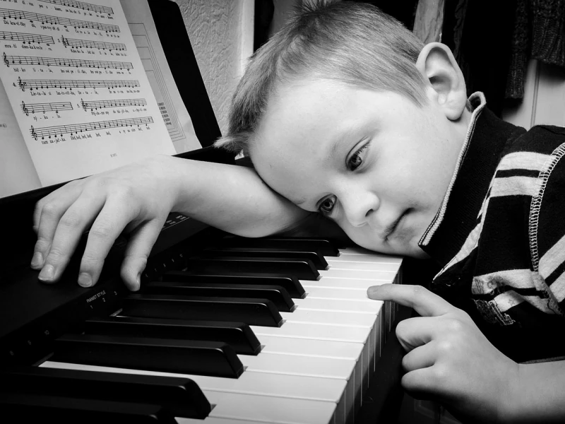 Ein Kind liegt mit seinem Kopf und einem Arm auf einer Klaviatur. Es hat einen Finger auf eine Taste gelegt und ist kurz davor, die Taste herunterzudrücken.